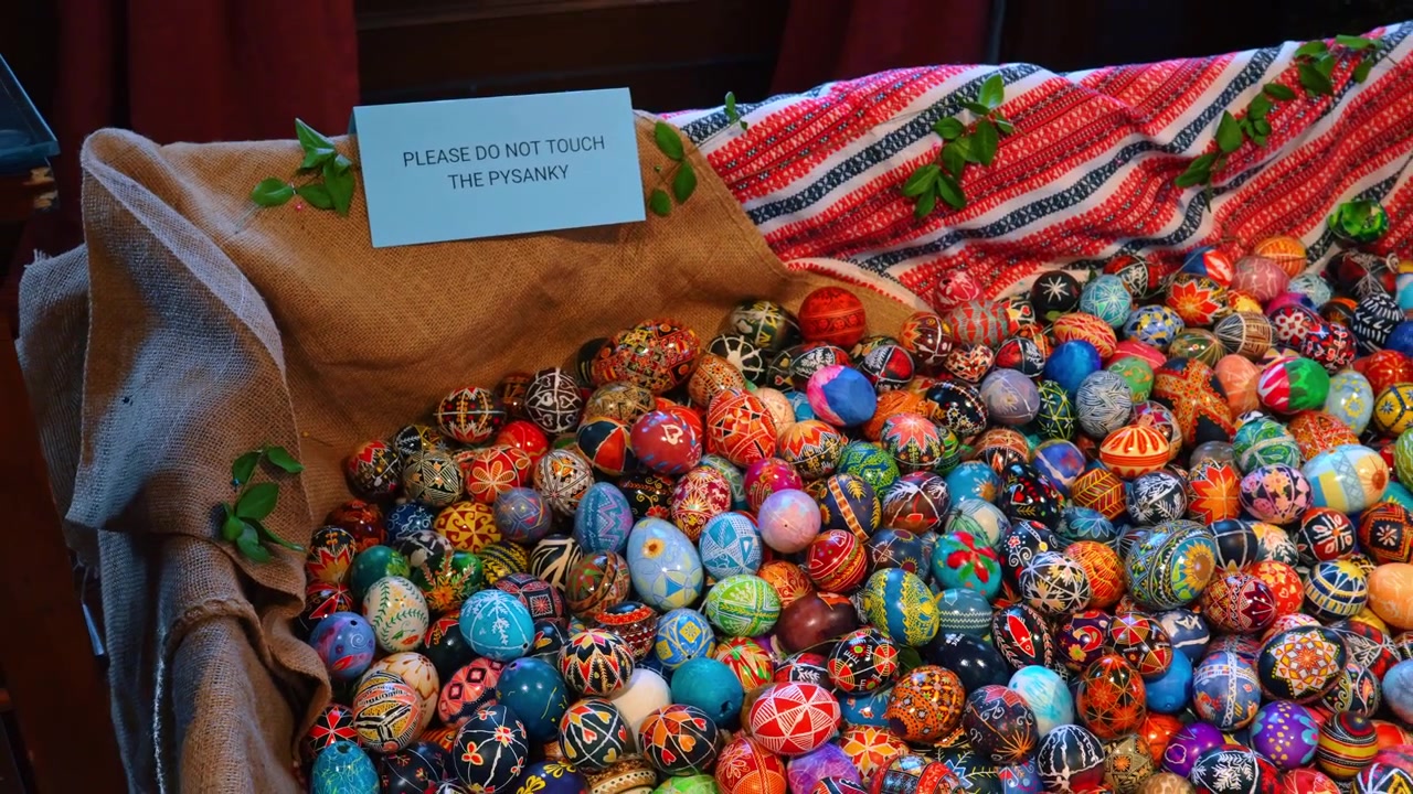 Collection of traditional Ukrainian Pysanky Easter eggs on burlap. Large pile of hand-painted Pysanky eggs with intricate patterns on brown burlap next to a warning sign in New York.