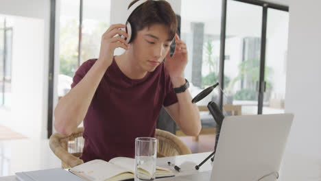 asian boy wearing headphones speaking on professional microphone to record audio podcast at home