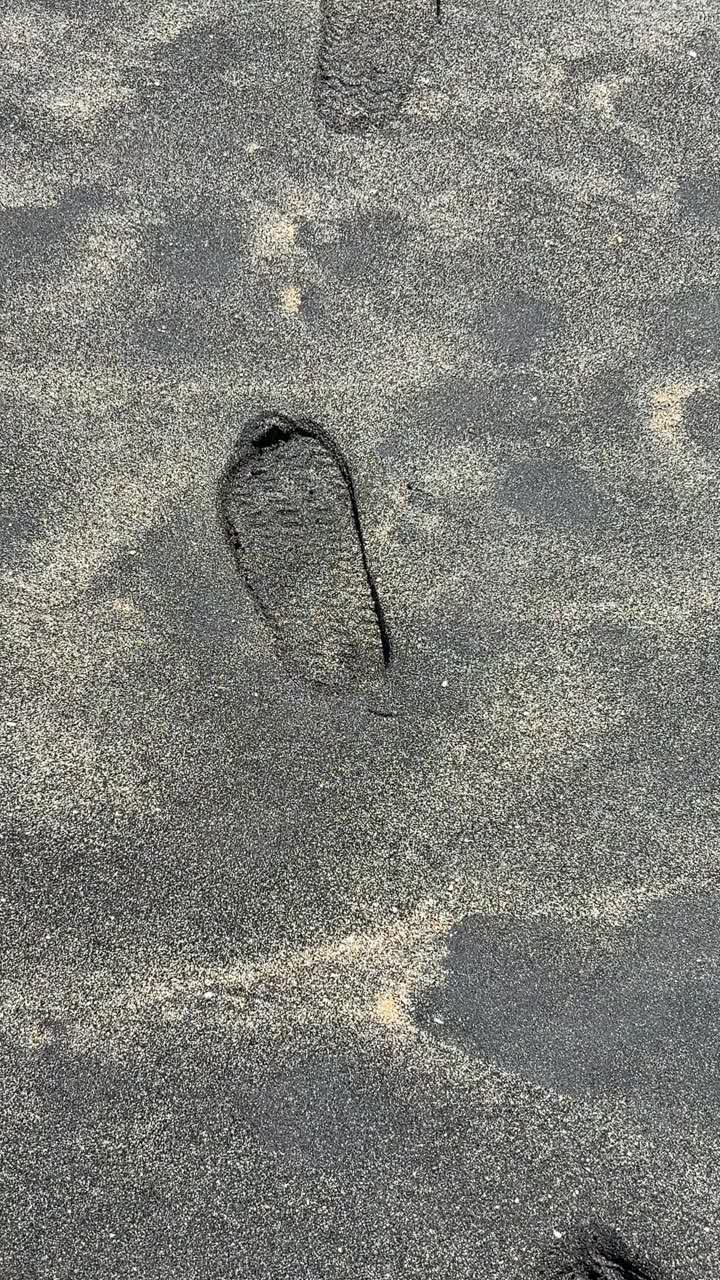 Primer plano de huellas en arena oscura en una playa