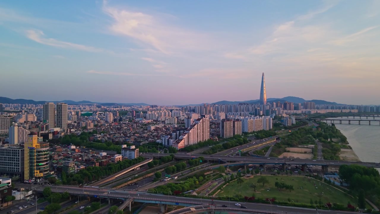 Sorvolo aereo sopra il Parco Gwangnaru Hangang, i ponti Gwangjin e Cheonho sul fiume Han verso la Lotte World Tower al crepuscolo a Seul