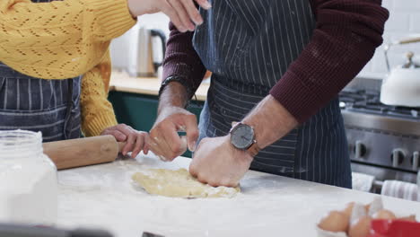 Midsection-of-diverse-couple-baking-christmas-cookies-in-kitchen-at-home,-in-slow-motion