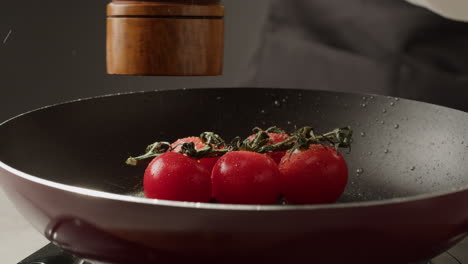 chef seasoning cherry tomatoes in a pan