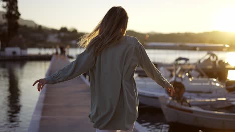 blonde woman walking along marine bridge, happily whirling around