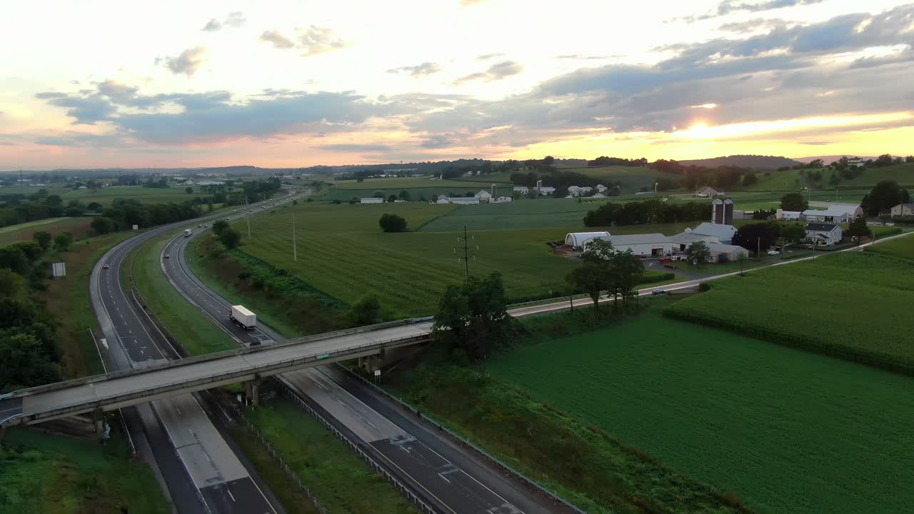 극적인 일출 아래 고속도로에서 자동차와 트럭, 여름 동안 녹색 시골 미국 농지 사이에서 일몰, 교통 공중 상승