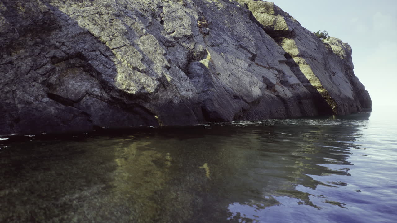 Nature reflecting on calm water beside rocky shoreline at dawn