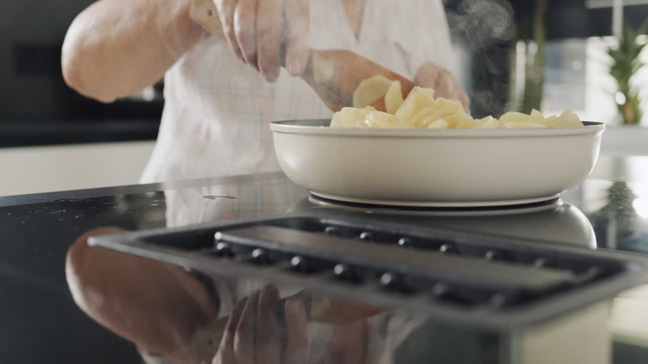 взрослая женщина жарит картофель на индукционной электрической печи с встроенным вентилятором.