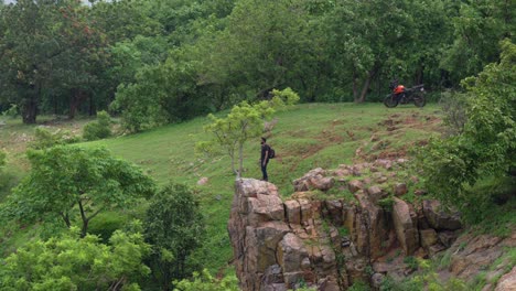 view of a young trekker looking at beauty of rainforest during monsoon with adventure bike at backgound. hiker standing on cliff edge.