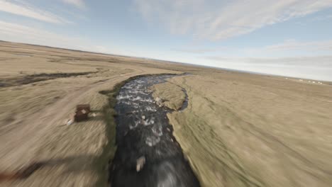 fpv aerial shot of stream and waterfall in an icelandic meadow