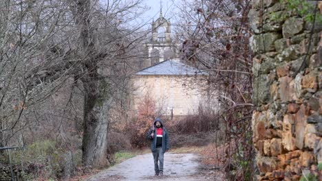 young man walks out of a rural church in the middle of the nature after a rainy day with a close umbrella on his hand