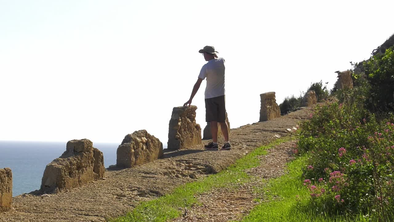 Man walking on cliff path, stops to look at ocean