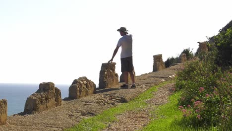 man walking on cliff path, stops to look at ocean