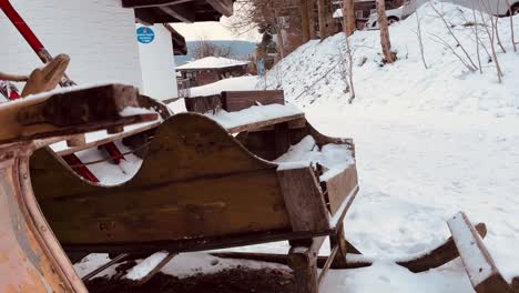 Old-wooden-sleds-stand-by-a-house-in-the-snow-with-trees-in-the-background