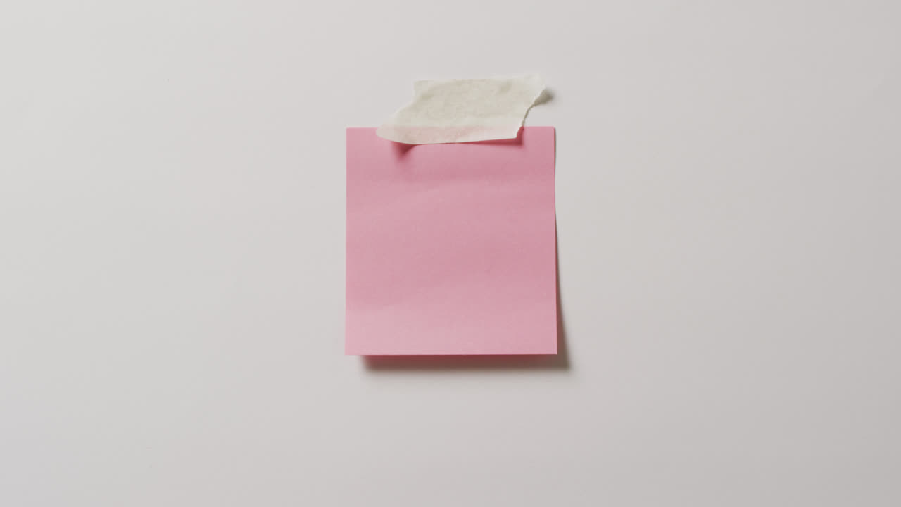 Video of close up of pink memo note with copy space taped to white background