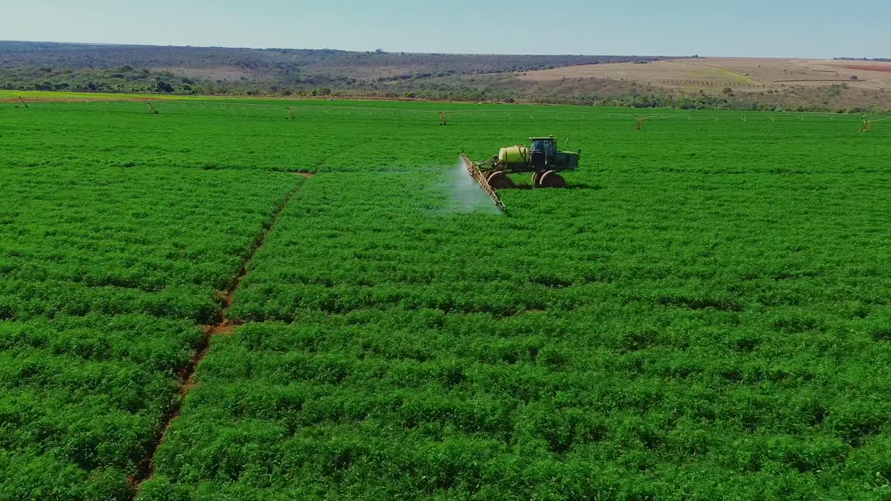 Vista aerea di un trattore che irrora le colture in un campo agricolo verde.