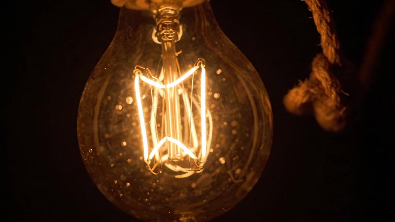 Lampadina vintage illuminata che irradia calore e carattere su uno sfondo scuro, mostrando un intricato design del filamento.