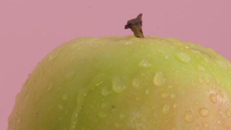 close-up of water drops flowing from a large green apple. fresh apple on a pink background. slow motion