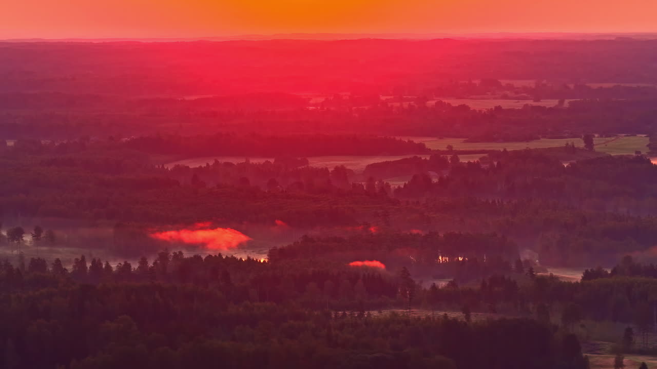 A stunning aerial shot captures an intensely vibrant and fiery red sunset casting a surreal glow over a vast, misty forest and lake landscape