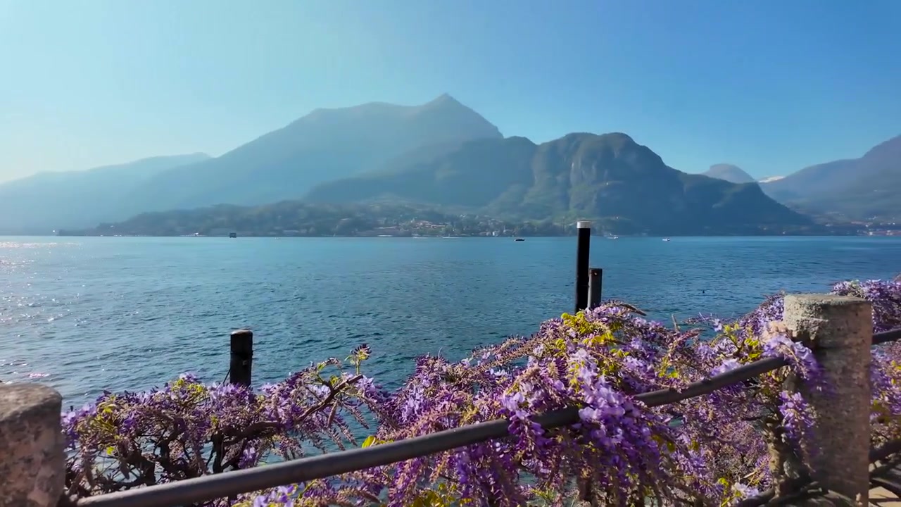 Vista panoramica sul lago a Bellagio, Italia, con affaccio sul Lago di Como, acque scintillanti, sagome di montagne, glicine in fiore e un tranquillo molo privato