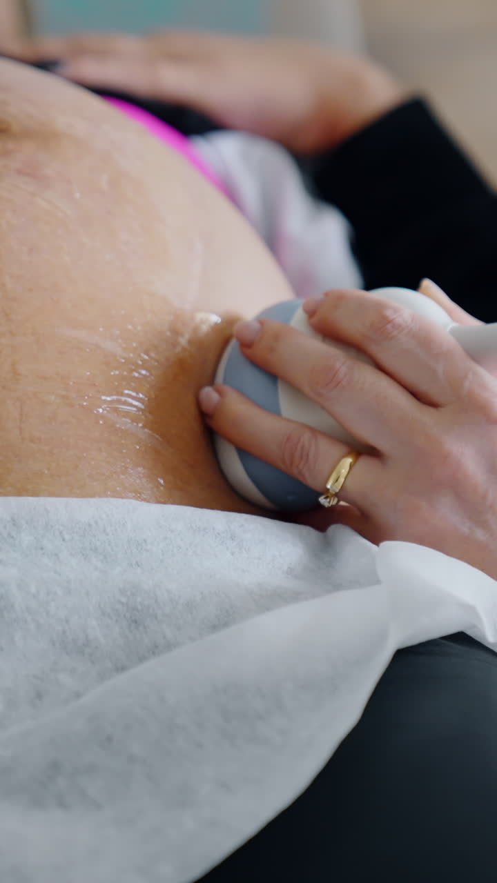 Pregnant woman is examined on the ultrasonic equipment. Medic holds the device on the big belly of a patient. Close up.. Vertical video