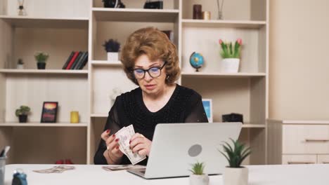 old-woman-is-counting-a-small-sum-of-dollar-bills-while-sitting-at-her-laptop