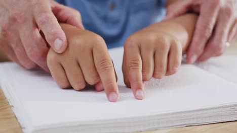 close up of caucasian grandfather and grandson sitting at table and reading braille, slow motion