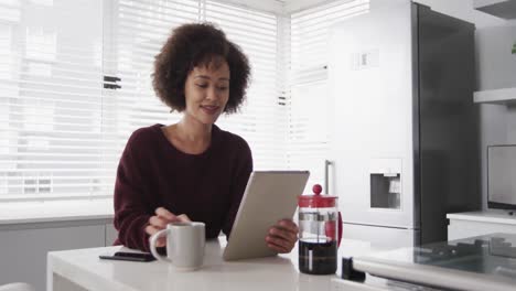 mujer usando una tableta digital y tomando un café en la cocina