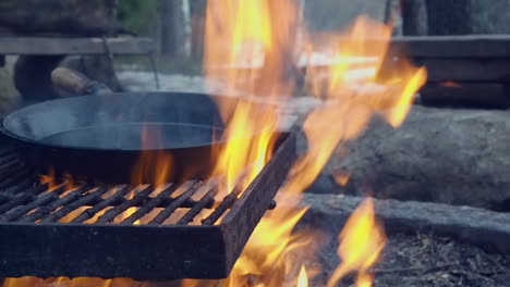 cast iron skillet smokes on a campfire grill over orange winter flames