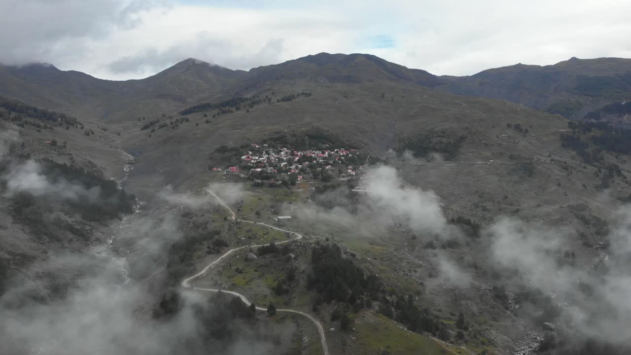estableciendo un video de drones de un antiguo pueblo en las montañas entre nubes y picos de montaña, un cañón de garganta a la izquierda del marco y caminos de montaña