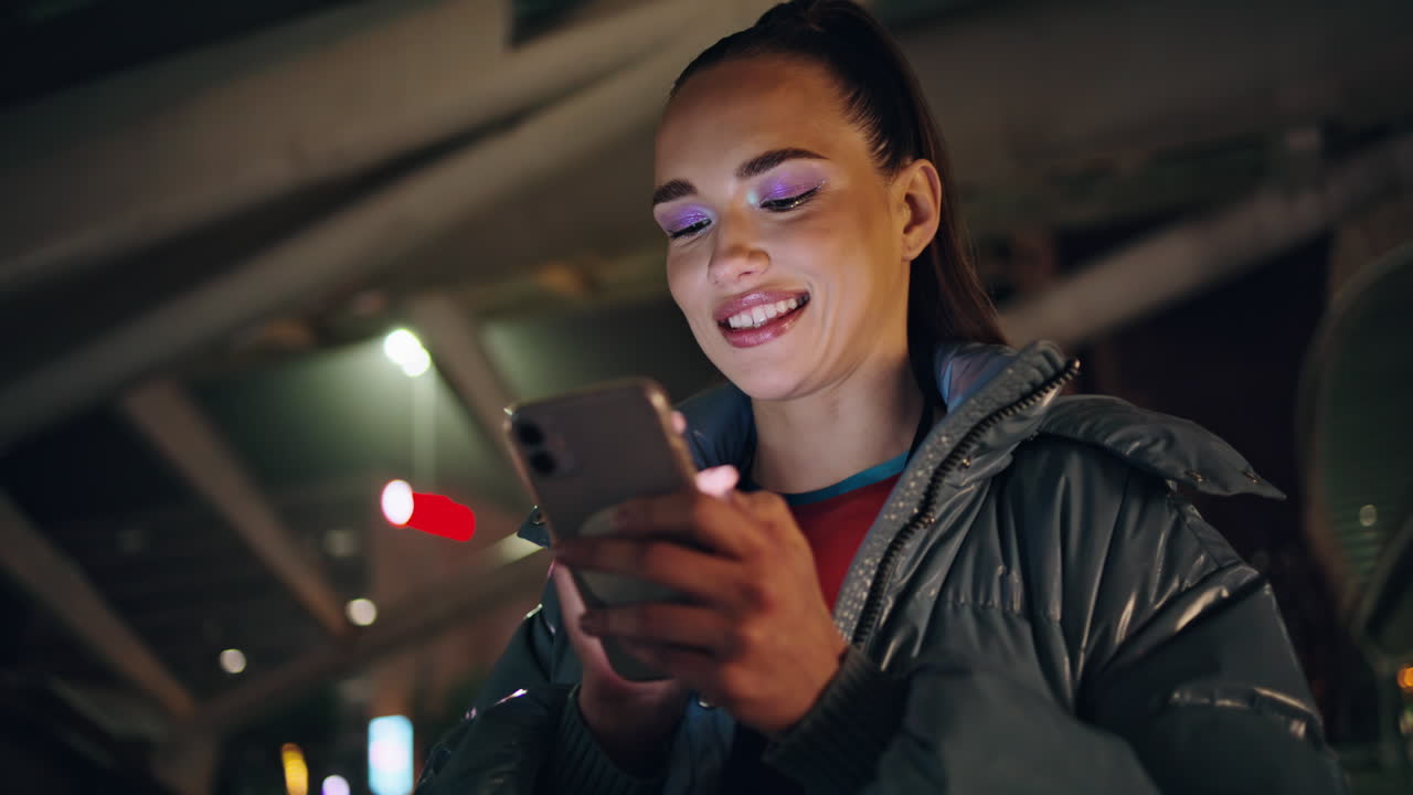 mujer feliz mensajería teléfono inteligente de pie con luces de la ciudad nocturna en el fondo.