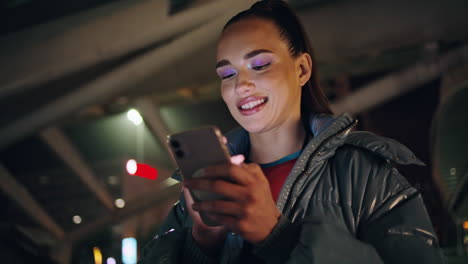 Mujer-Feliz-Enviando-Mensajes-A-Un-Teléfono-Inteligente-De-Pie-Con-Las-Luces-Nocturnas-De-La-Ciudad-Como-Telón-De-Fondo.