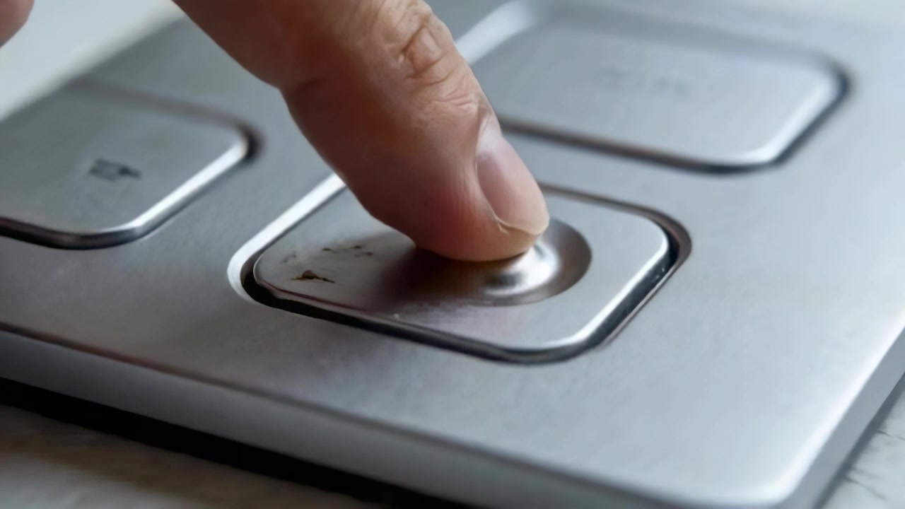 Approaching adult fingertip pressing recessed button on silver panel, depressing circular center