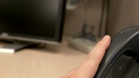 a close up of a hand picking up and slamming an office phone down a couple of times onto the phone base in an office cubicle