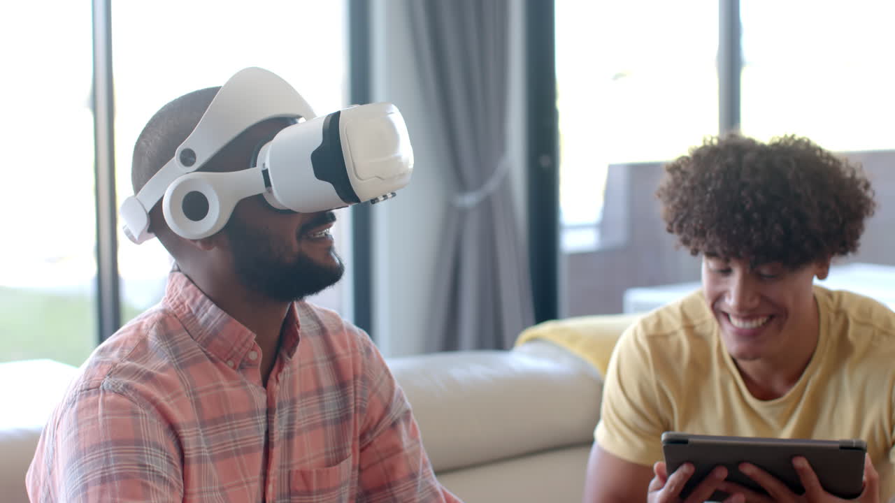 Using VR headset, man enjoying virtual reality experience with friend holding tablet