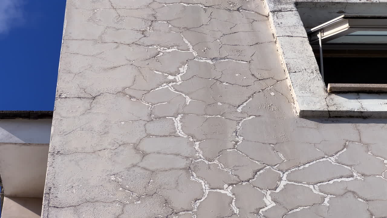 Primo piano di intonaco esterno screpolato con vernice scrostata, sfondo con texture di superficie di facciata deteriorata.