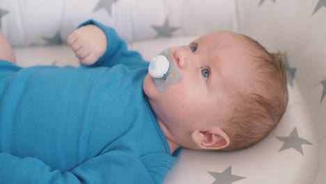 funny little boy rests sucking dummy in sleeping cocoon