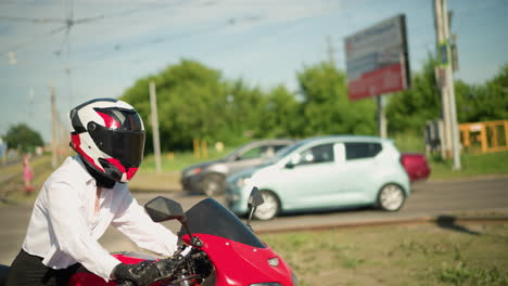 a female motorcyclist on a red bike makes a turn while a white car drives by with other cars coming from behind and pedestrians are visible in the blurred background