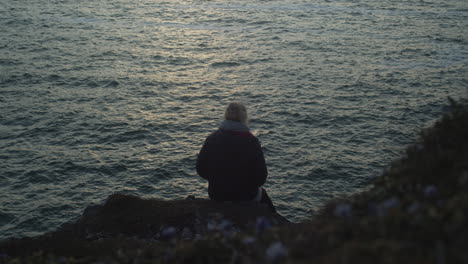 Mujer-Sentada-Al-Borde-De-Una-Colina-Con-Vistas-Al-Mar-Al-Atardecer---Plano-Medio