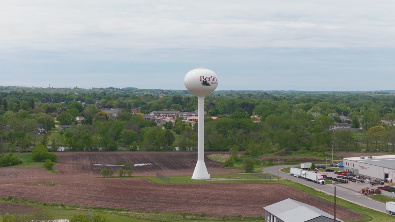 Torre dell'acqua di Berlino, Wisconsin, che si erge sopra le cime degli alberi primaverili, case e campi agricoli ai margini della città