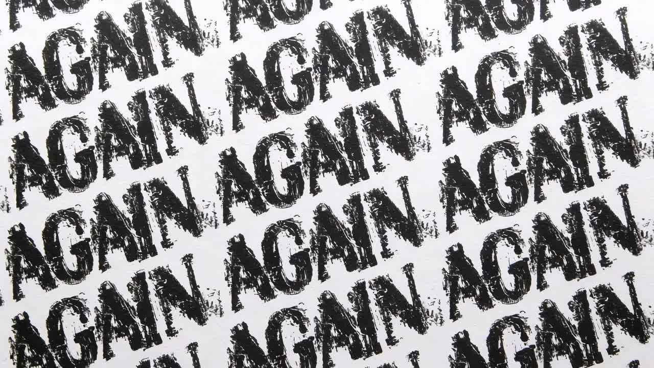 Moving camera capturing close-up repeating AGAIN stamps on white sheet, showing ink texture