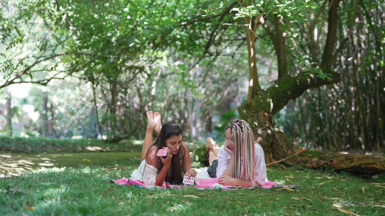 Two women playing cards on a picnic in a park