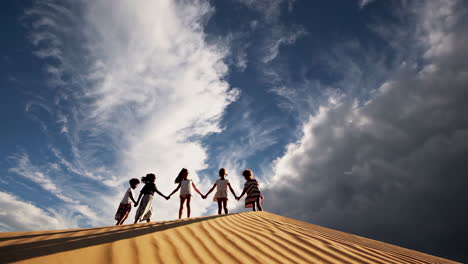 children holding hands on a sand dune under a cloudy sky