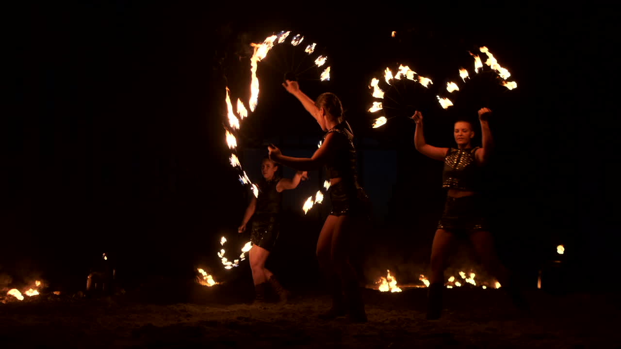 cámara lenta: actuación de fuego profesional tres mujeres con ropa goteante bailan y giran con antorchas en llamas y un hombre con lanzallamas en el fondo.