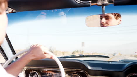 young white man driving an open top car, face seen in mirror