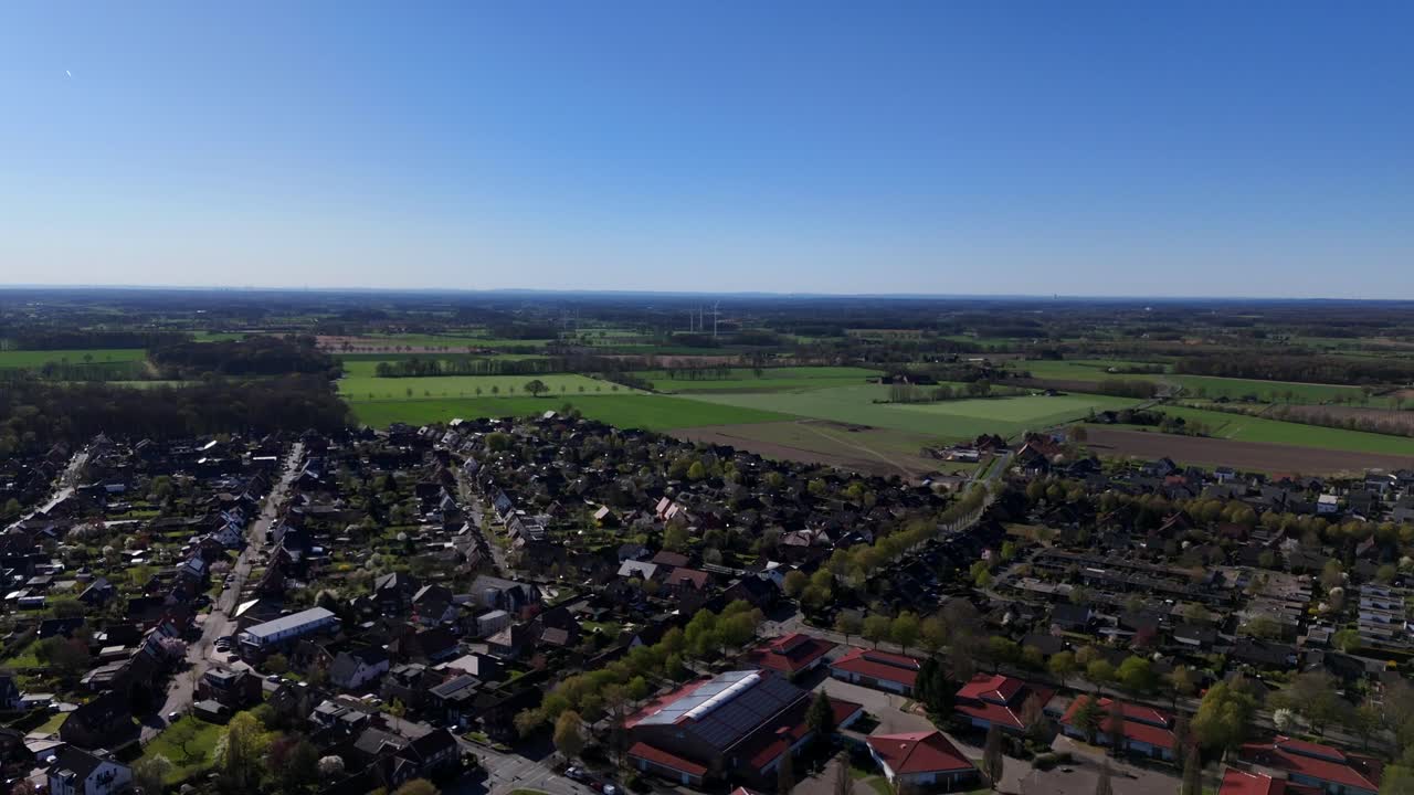 American city with green Farm fields on sunny spring day. Streets with single family houses and school campus. Aerial forward wide shot.