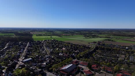 american city with green farm fields on sunny spring day. streets with single family houses and school campus. aerial forward wide shot.