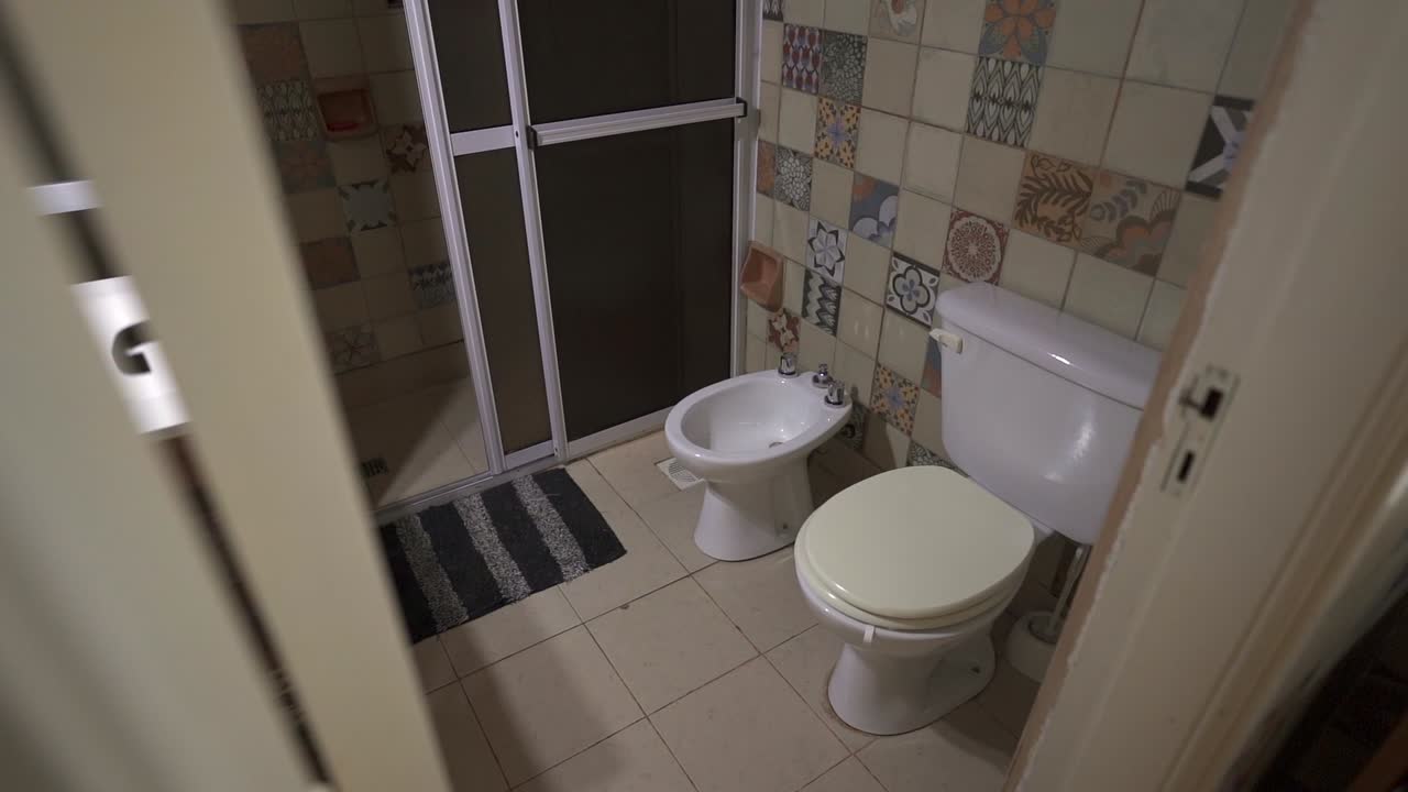 Small tiled house bathroom with toilet and bidet next to sliding shower door.