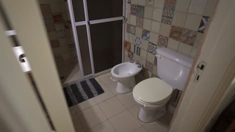 small tiled house bathroom with toilet and bidet next to sliding shower door.