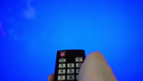 mano masculina con el control remoto apuntando a la pantalla de la televisión. llave de croma azul.
