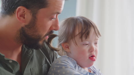 Cerca-De-Un-Padre-Con-Síndrome-De-Down,-Una-Hija-Leyendo-Un-Libro-Y-Riéndose-Juntos-En-Casa