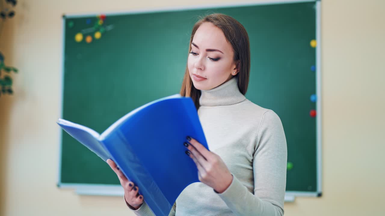 Beautiful teacher with a folder. Pretty young woman holding a blue folder and looking at files on the background of a board. Education concept.
